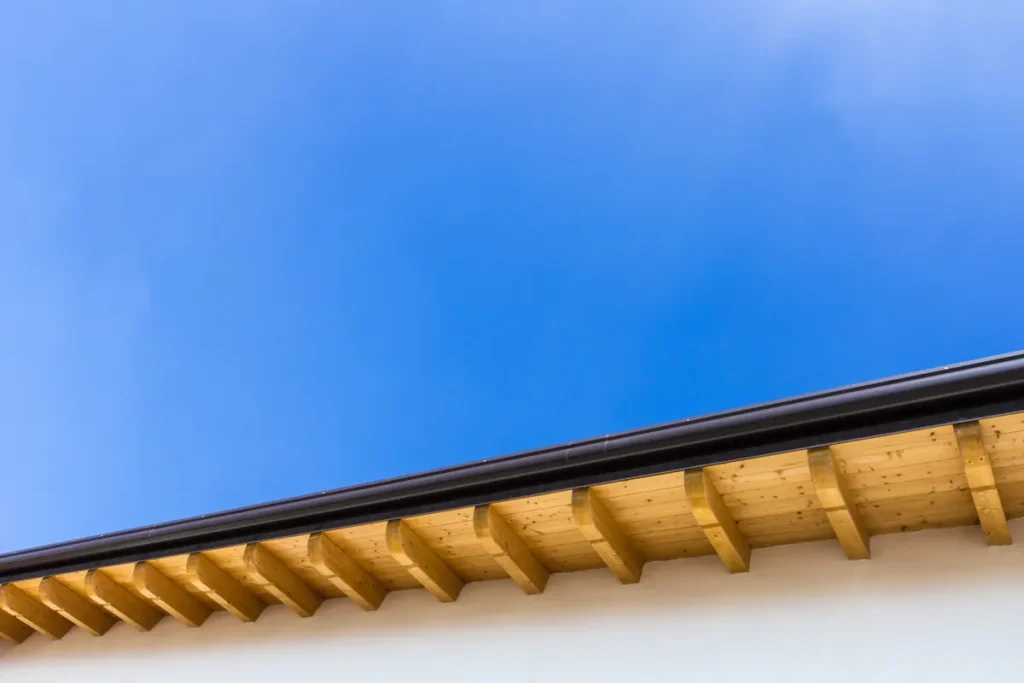 Avant-toit en bois et chevrons d'une maison sous un ciel bleu